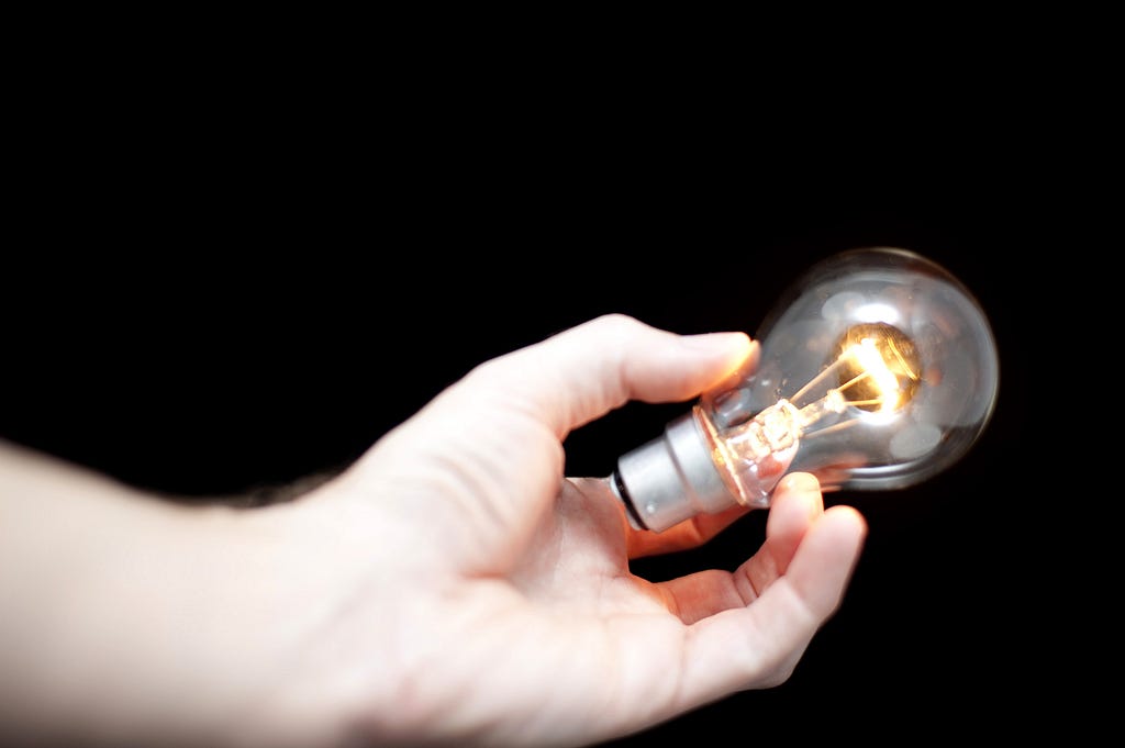 An arm coming in from the left holding a burning lightbulb, on a black background.