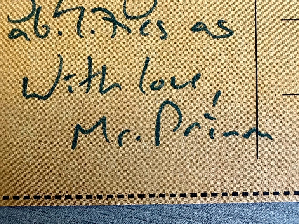A macro image of a cardboard postcard. Handwritten text reads, “With love, Mr. Primm”.