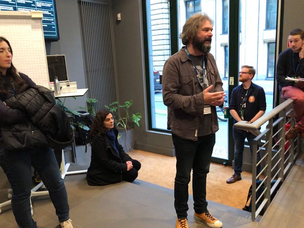 Vasilis van Gemert standing up, surrounded by his audience, talking about the design of assistive technology.