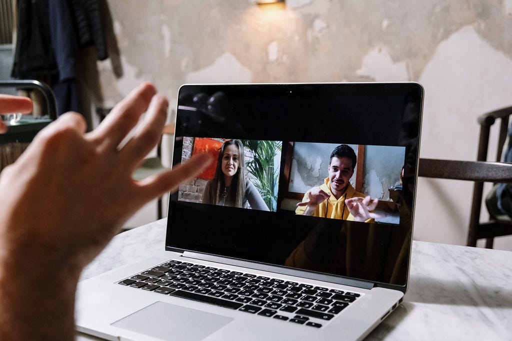 A laptop computer screen showing a video call with two other people using sign language to communicate with a third person that is not pictured