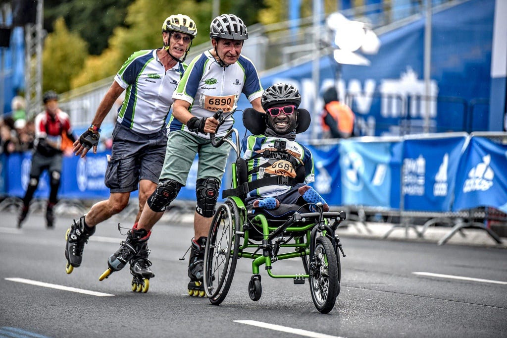 Three men, one in a wheelchair, two on roller skates taking part in a marathon together.