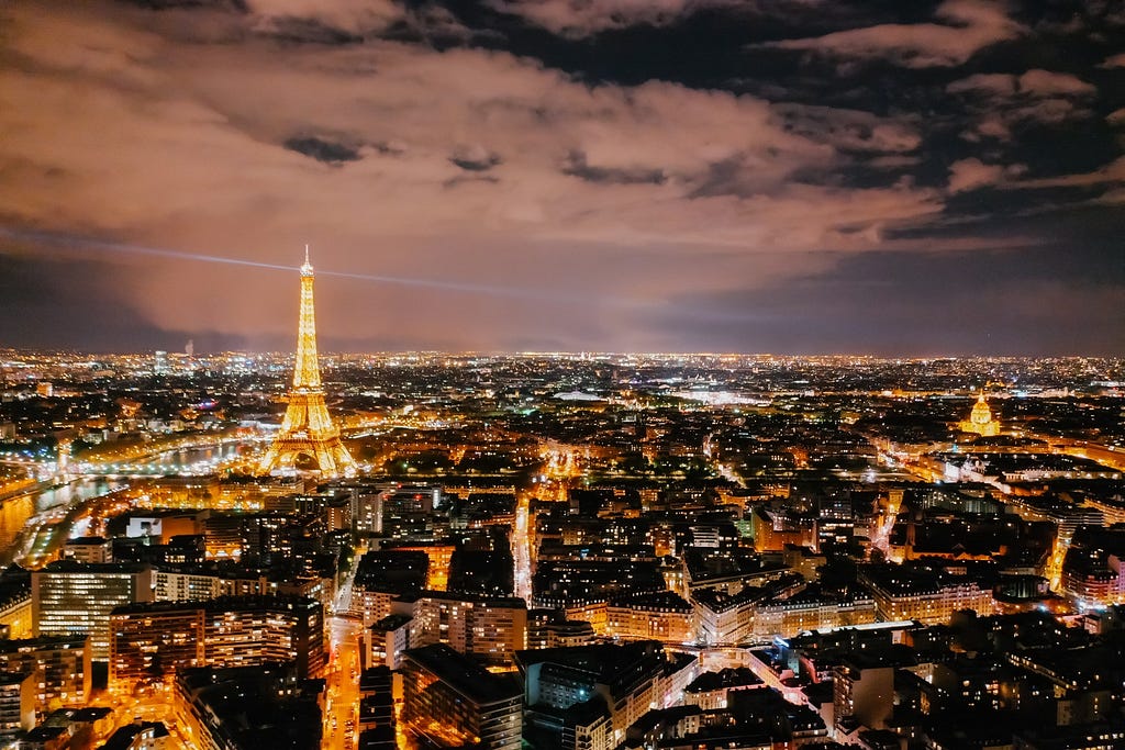 The city of Paris at night, with the lit up Effiel Tower being prominent, as well as the numerous lights of the various buildings that surround it.