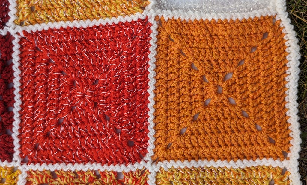 Left square is made out of red yarn with strands of white embroidery floss peeking through all the stitches. Right square is made out of orange yarn with no white embroidery floss.