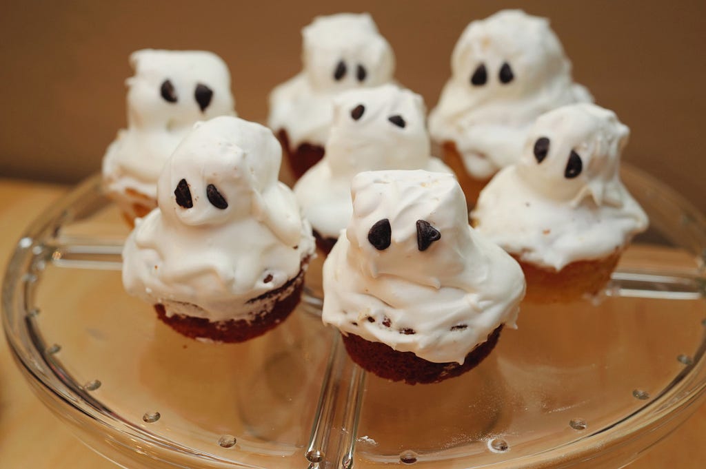 Cupcakes with white icing and marshmallow toppers with black icing dots for eyes made to look like ghosts