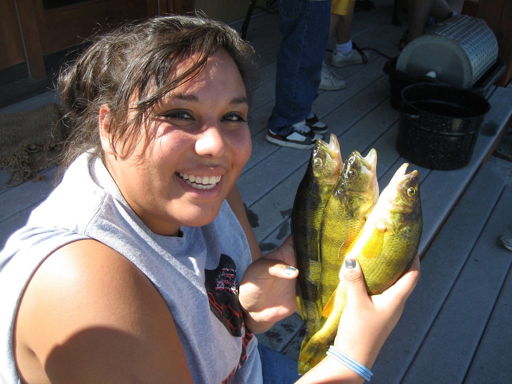 Native American teenager smiles and holds three yellow green perch she caught