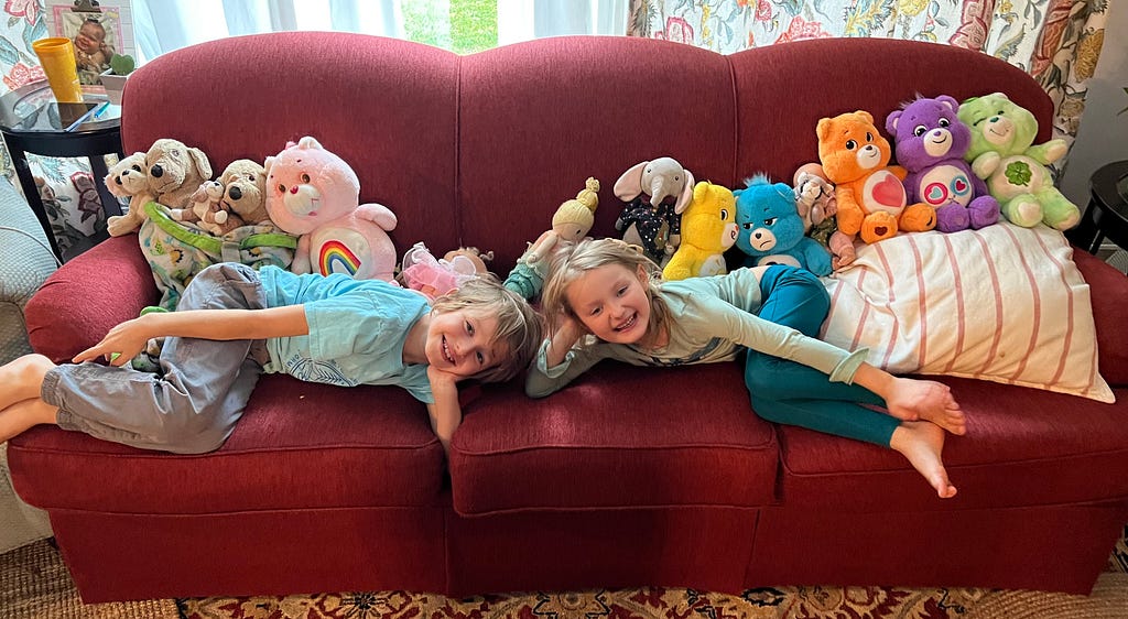 Two kids laying out a couch with their stuffed animals.