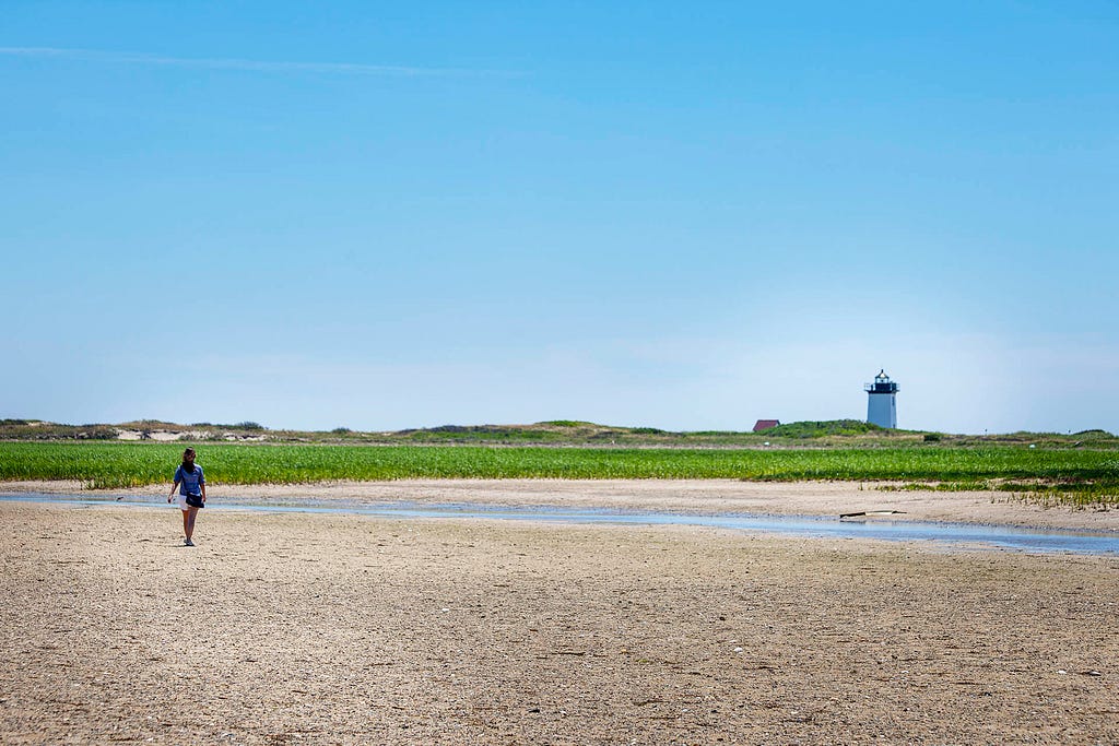 a lady walking towards a distant lighthouse across a sandy area