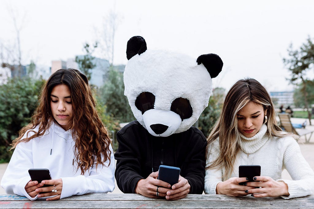 Three people staring at their mobile phones. One is wearing a panda costume head.