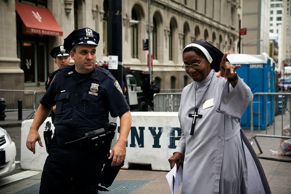 A police officer and a nun in an urban environment. The nun is pointing a direction.