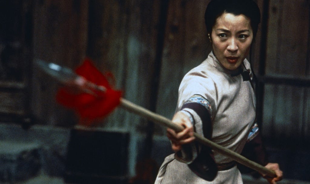 A woman dressed in a beige martial arts outfit holding a spear.
