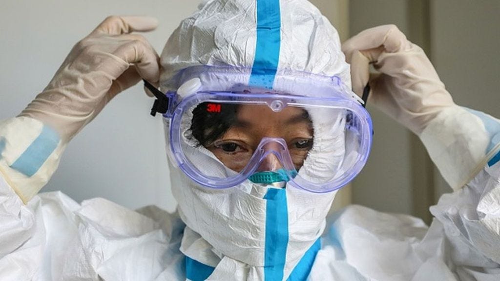 A nurse removing her eye shield while her full-body gown is still on