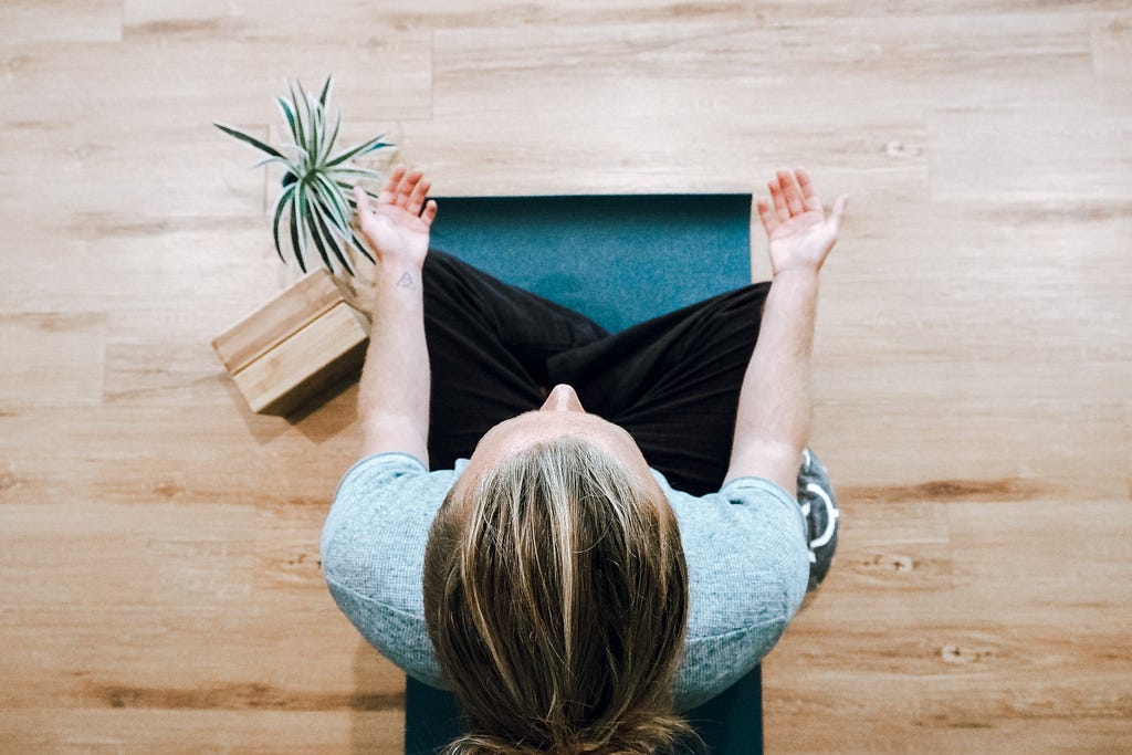 View from above of a woman sitting on a yoga mat, meditating.