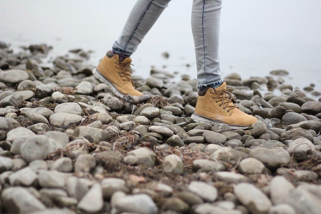 Lower part of person’s legs in walking boots, walking along a stony shore to water