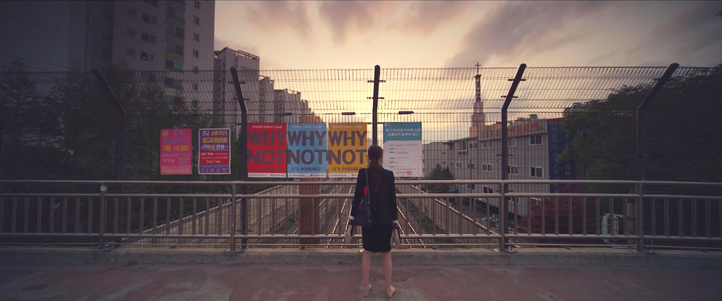 Koo Se-ra stands on an overpass, staring a a series of posters that say “Why Not?”