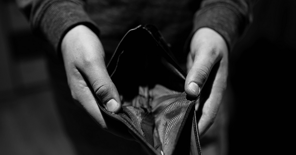 A monochromatic image of a person’s hands holding an empty wallet.