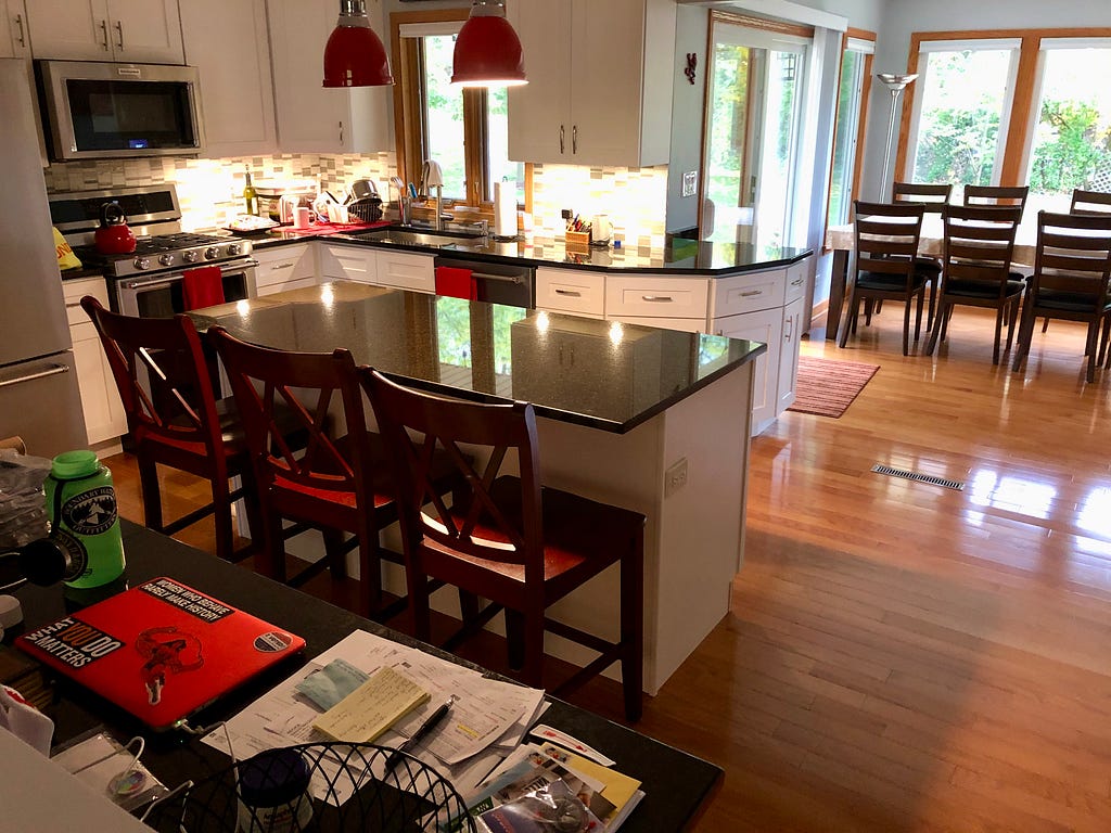 Author’s photo of her kitchen: cluttered counter, cleared off kitchen island, appliances, kitchen table.