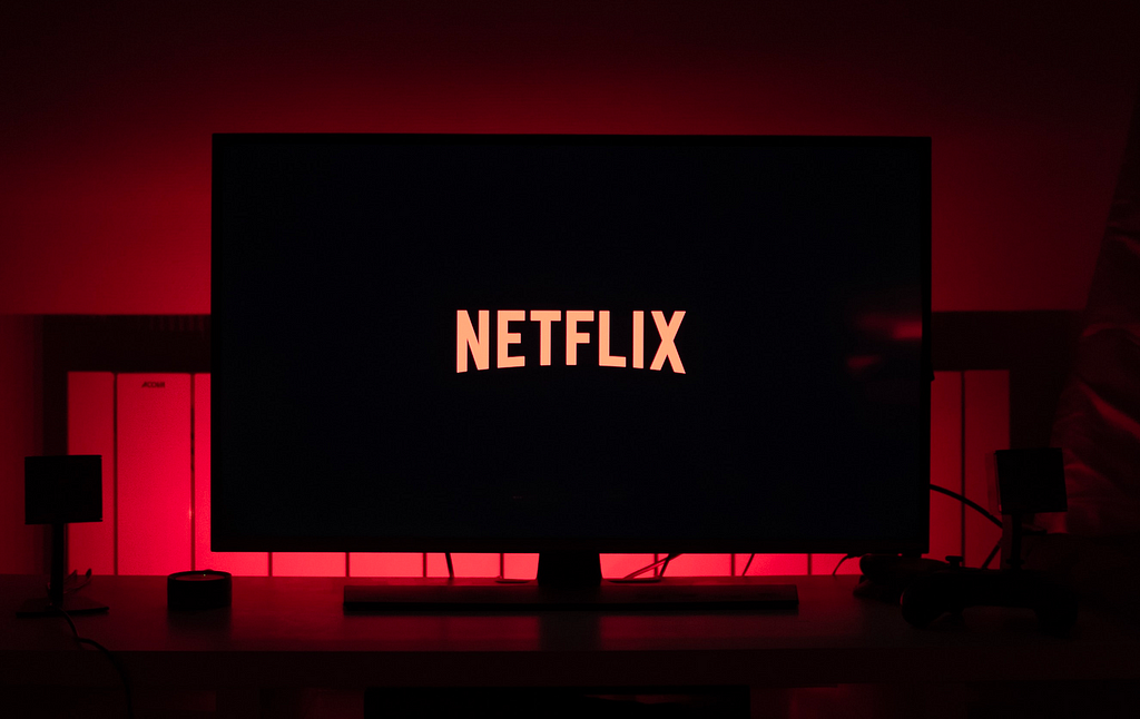 Netflix logo on a computer screen in a dark room, with red light glowing behind the screen.