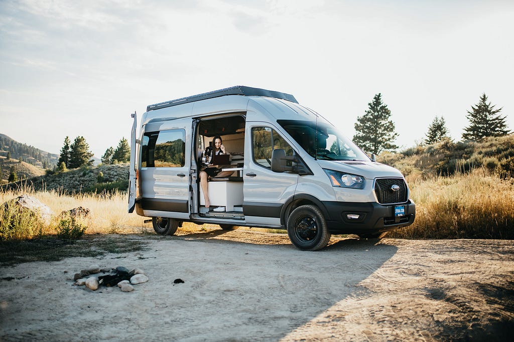 Ford Transit camper with side door open and lady working on a laptop living vanlife