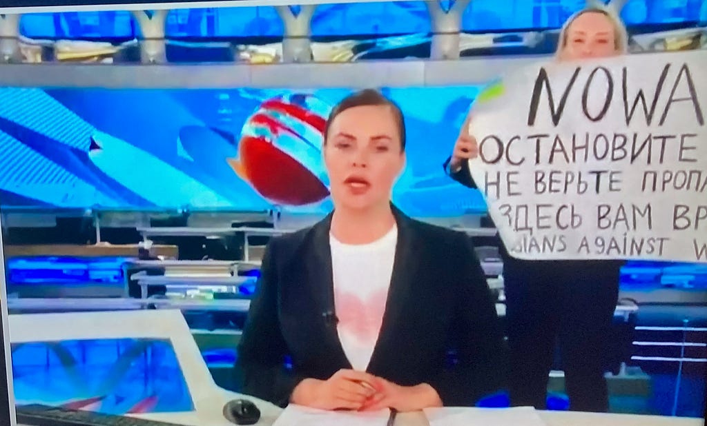 Editor-producer Marina Ovsyannikova holds protest sign behind female anchor on Russian state television news program on Channel One.