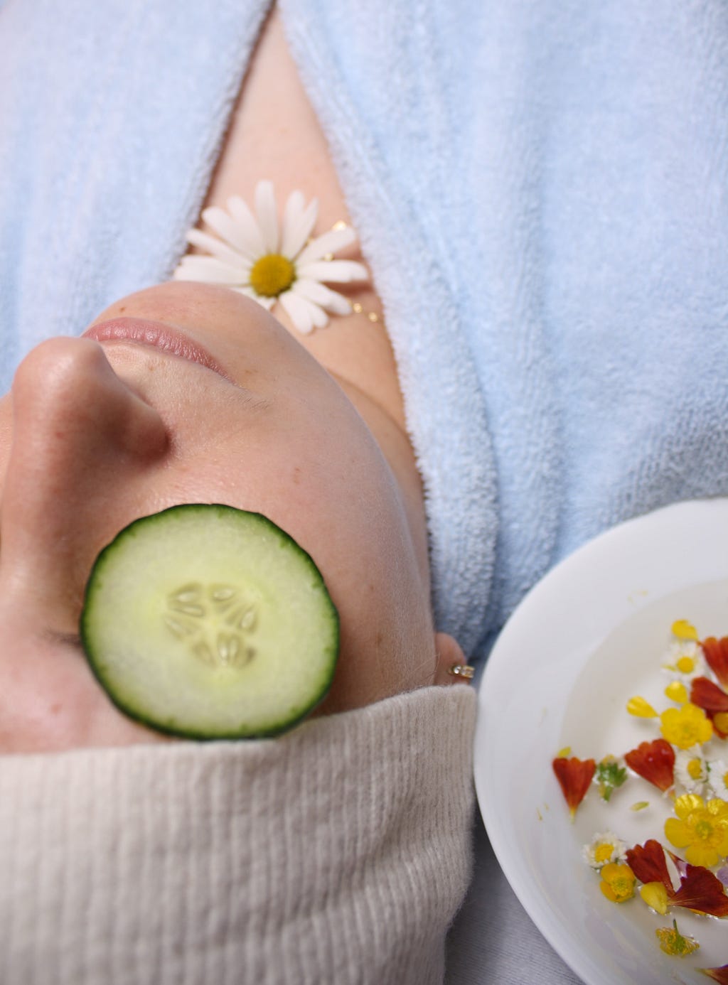 photo of woman with cucumber on eyes and flower on chest wearing blue robe; photo on Dr. James Goydos 2021 article on skin care self care and skin cancer prevention