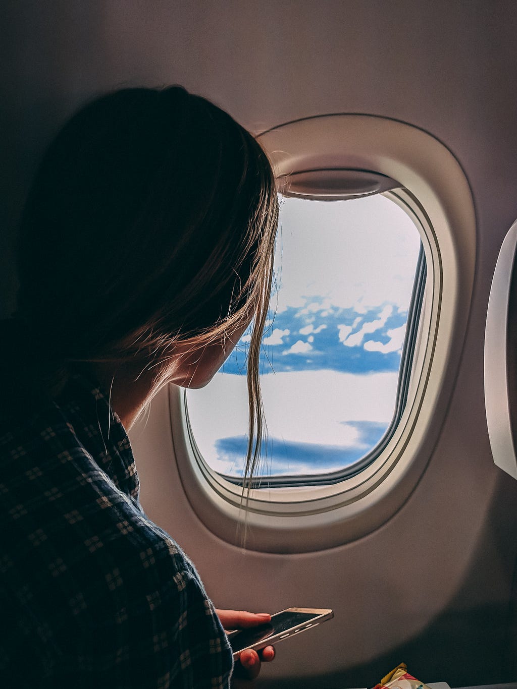 girl holding smart phone looking outside airplane window
