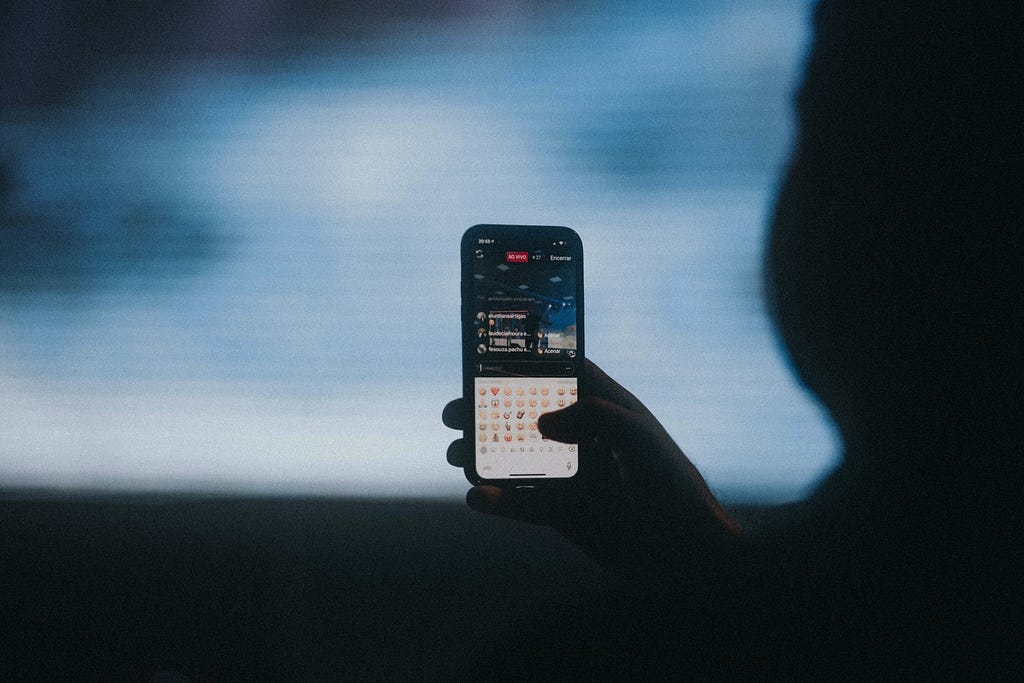 A cell phone on which Instagram live is being watched and the emoji keyboard is opened.