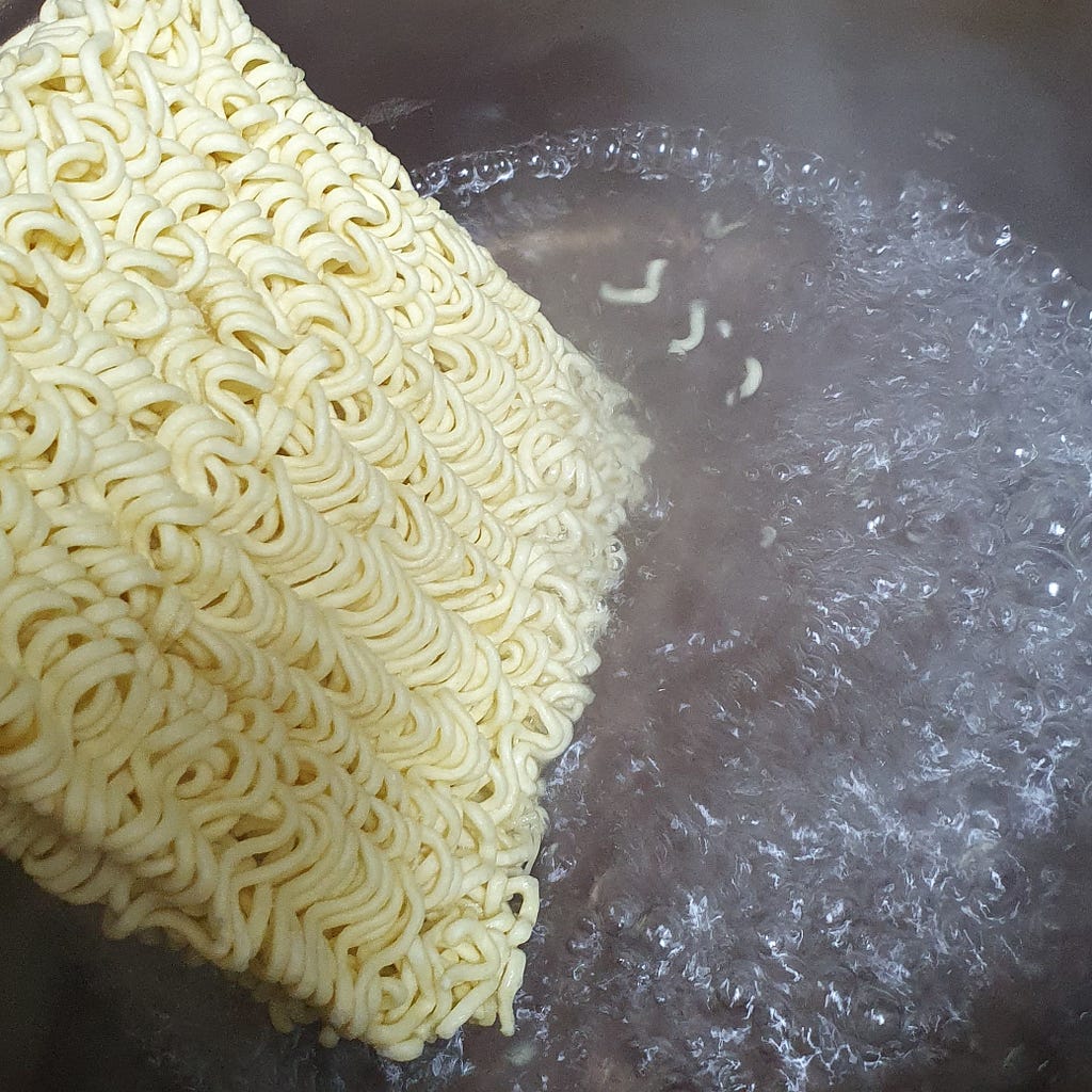 Adding the instant ramen noodles to a boiling pot of water for a package of Wicked Ramen (Yogoe Ramyeon) Shinsadong Naengcho-Myeon Flavor.