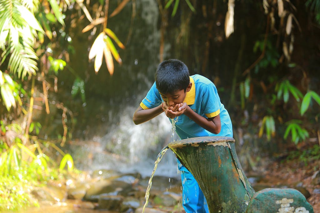 Indian boy blue clothing drinking water from an open pipe in a jungle