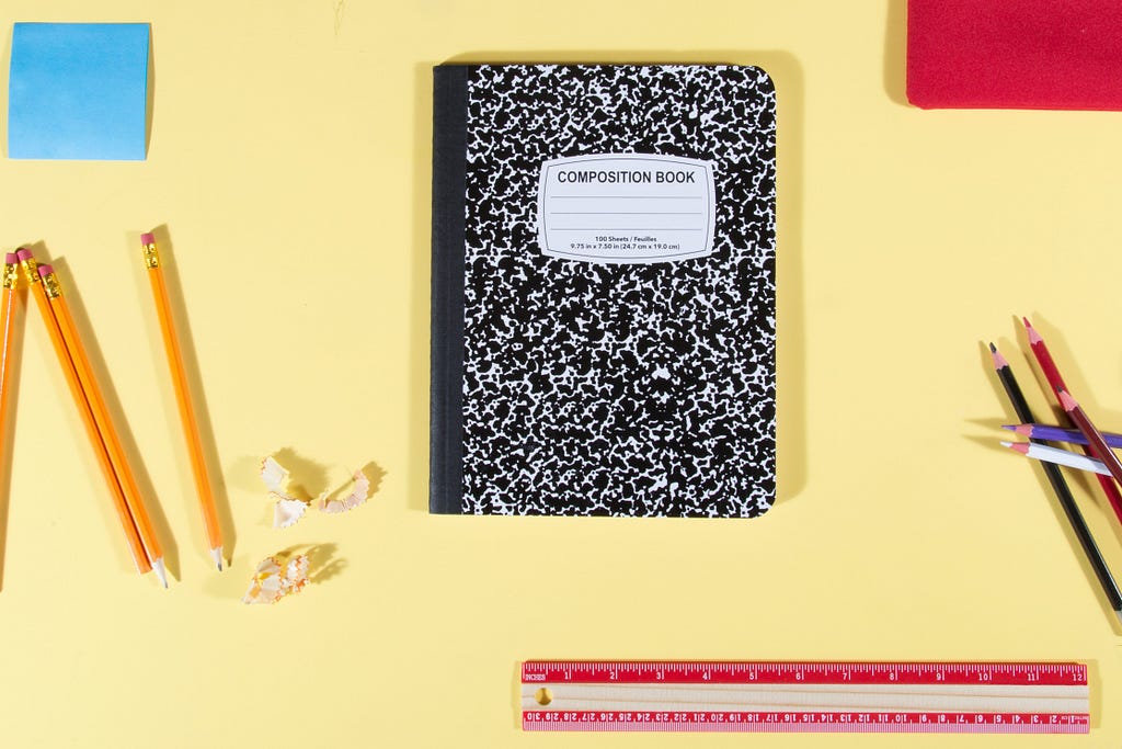 closed note book and pencils on a yellow desk top