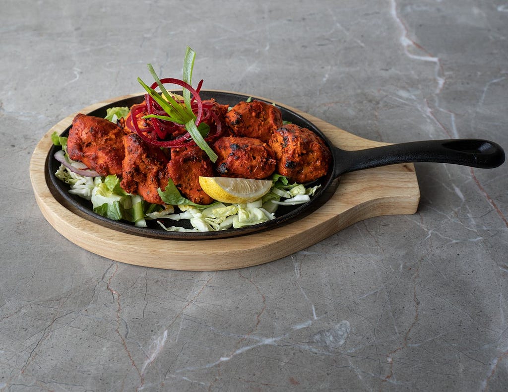 A serving of tandoori chicken on a hot plate