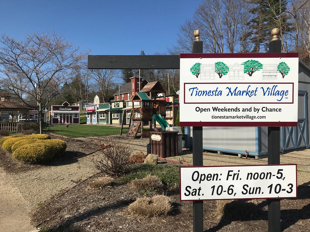 The exterior of the market village shows the sheds and a play area. A sign says “Tionesta Market Village, open weekends and by chance”
