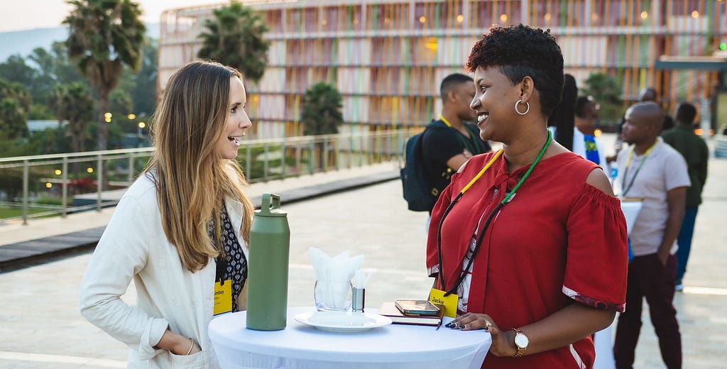 A white woman and a black woman smile and talk together over a cocktail table