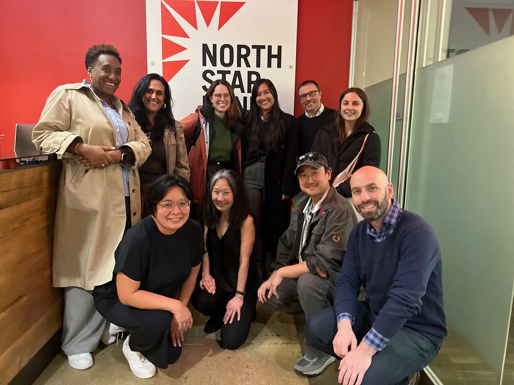 Ten people stand in front of the North Star Fund logo. They are huddled together and smiling.