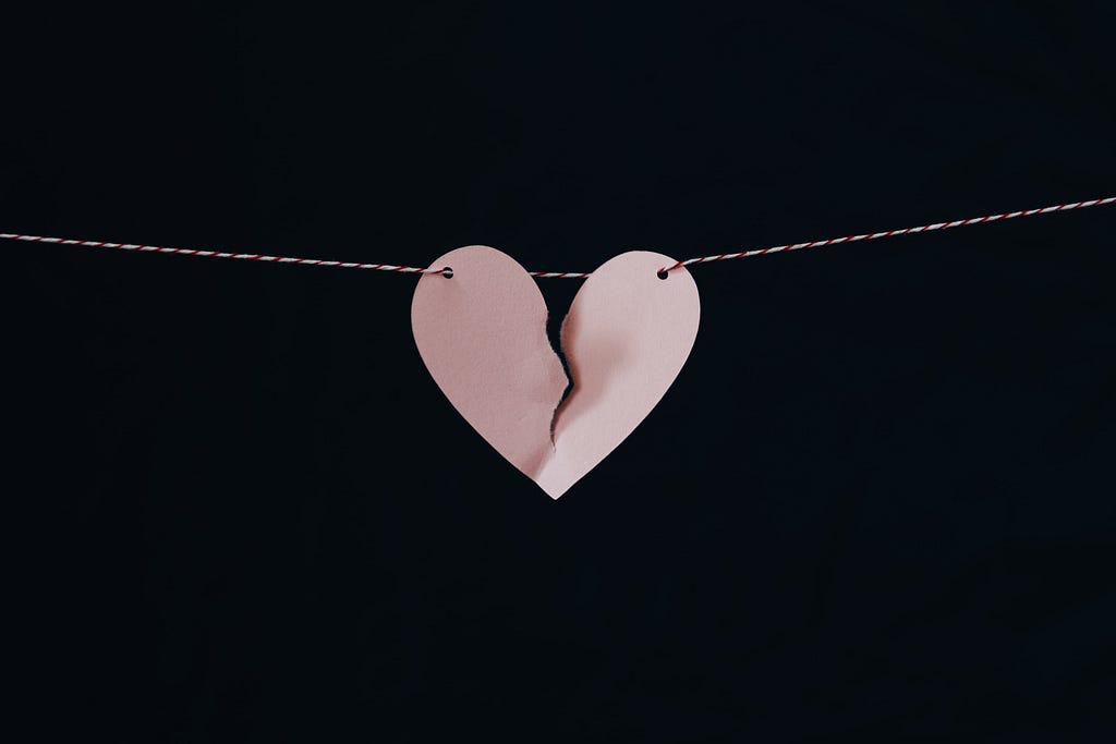 A paper heart hangs on a piece of string (like a clothes line). The paper heart has a tear through the middle.
