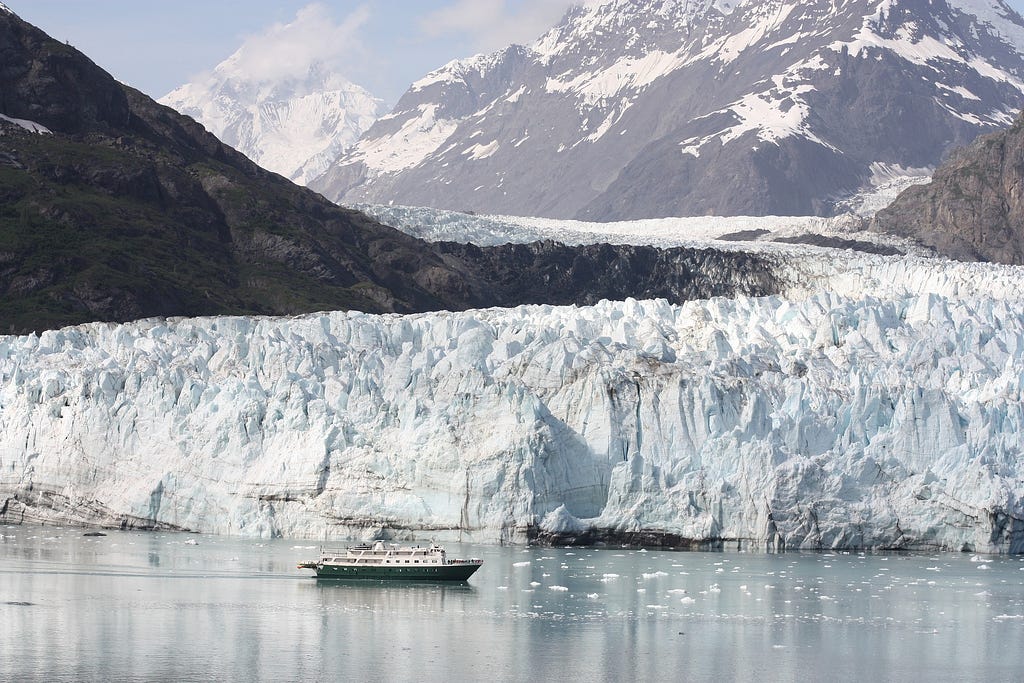 A ship in front of glaciers and mountains in Glacier Bay, Alaska.