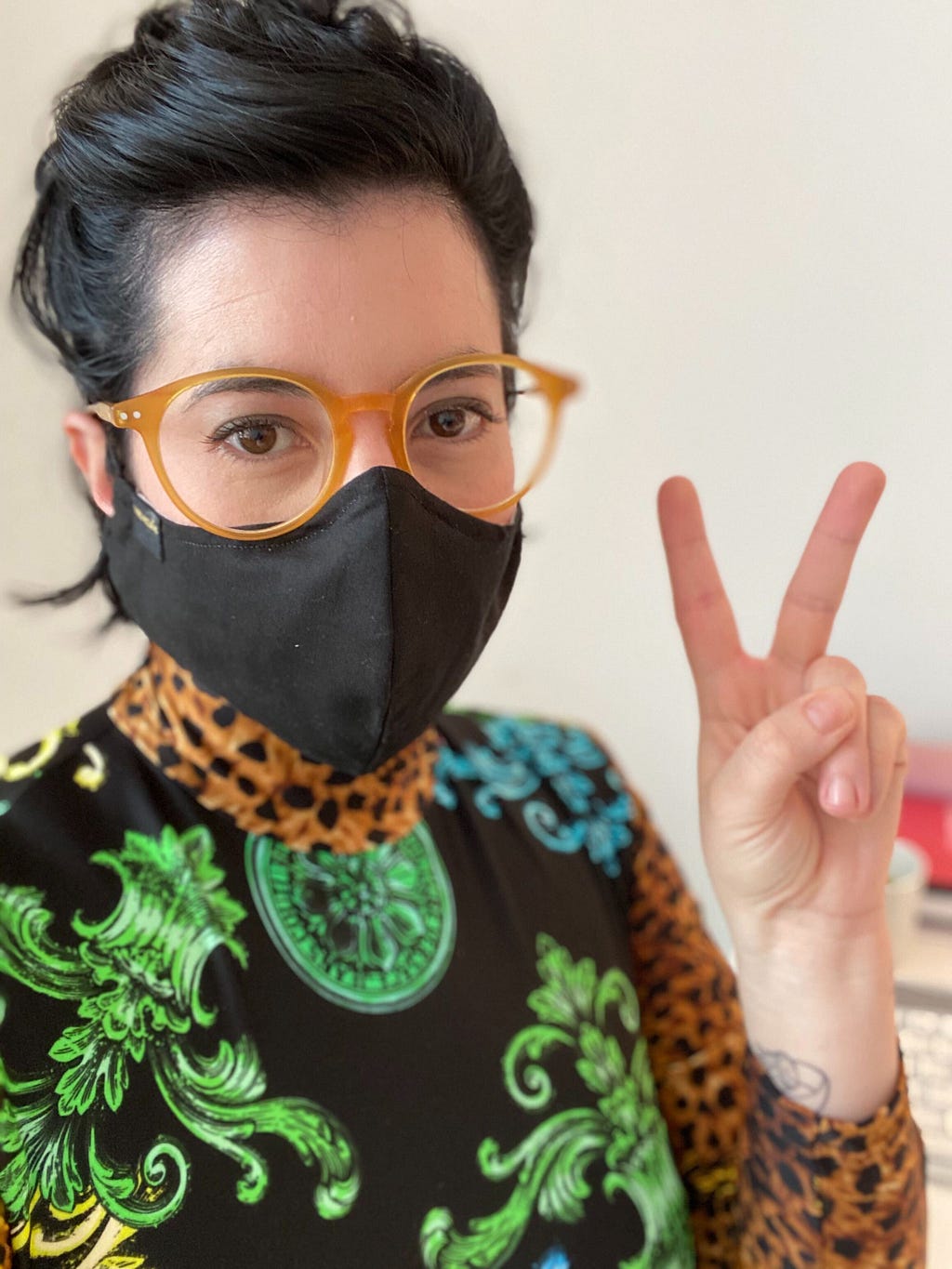 Woman wearing a black facemask and giving the peace sign.