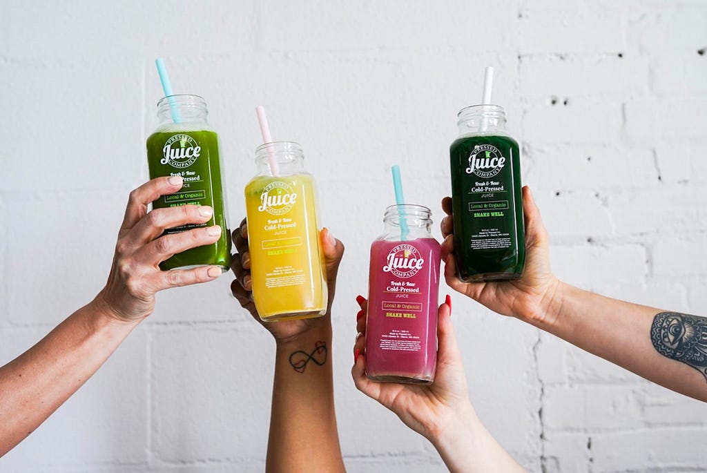 Photo of colourful juices in the cute bottles, held by hands.