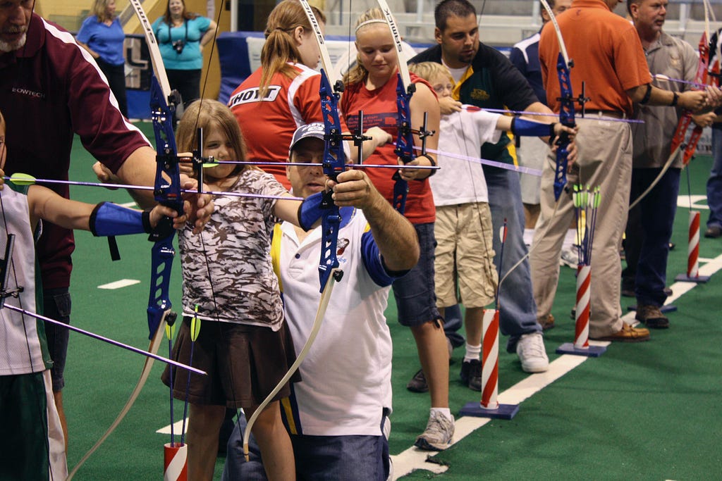 Young people being shown how to shoot a bow and arrow.