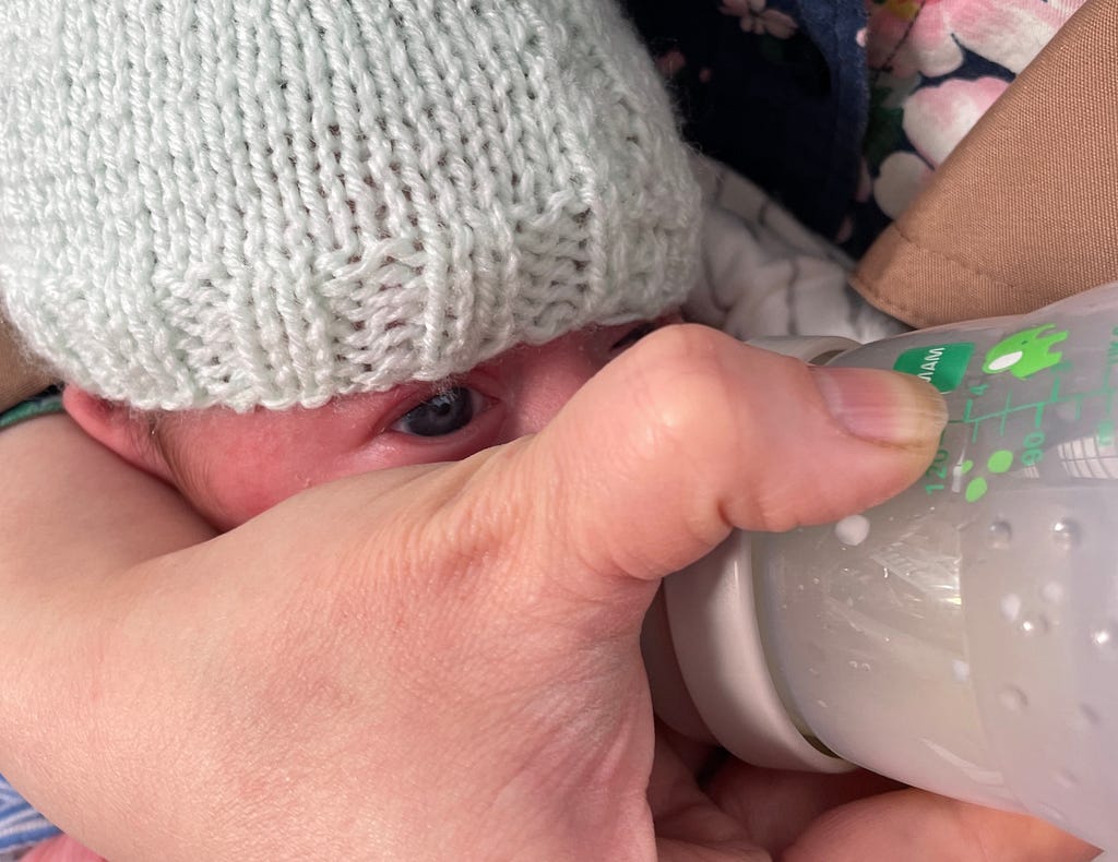 A baby hidden by a massive hand with a bottle
