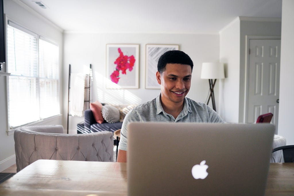 A young man on a laptop in his open-plan kitchen/living room. Image taken from Unsplash