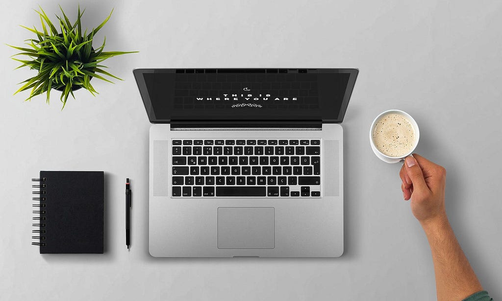 Looking down at laptop, notebook, and plant with person holding cup of coffee.