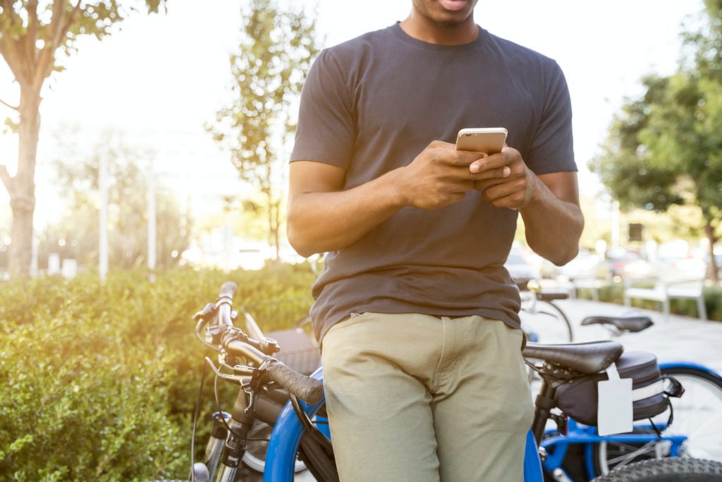 Man looking at phone during the day while leaning on bicycle