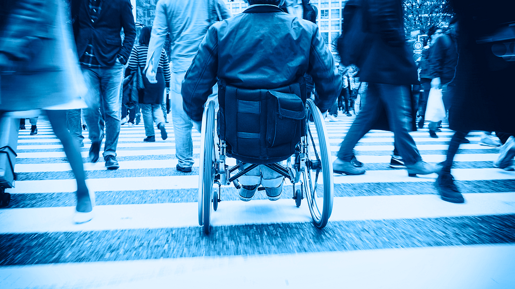 A person in a wheelchair using a crosswalk on a busy city street.