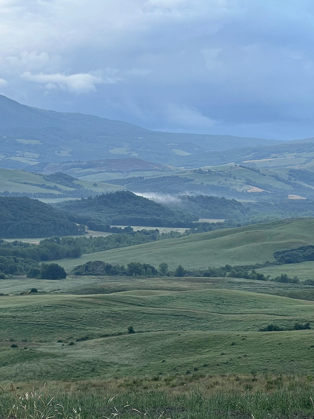 Photo of rolling Tuscan hills, the mist flowing between the peaks, the sky darkened with purple clouds