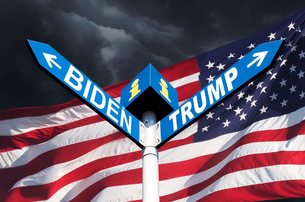 A pole with two arrows — one that says Biden, the other that says Trump — point in opposite directions in front of an American flag.