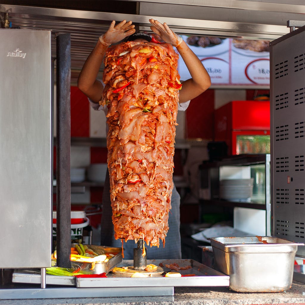 fresh gyro meat being looded on the cooking rotis