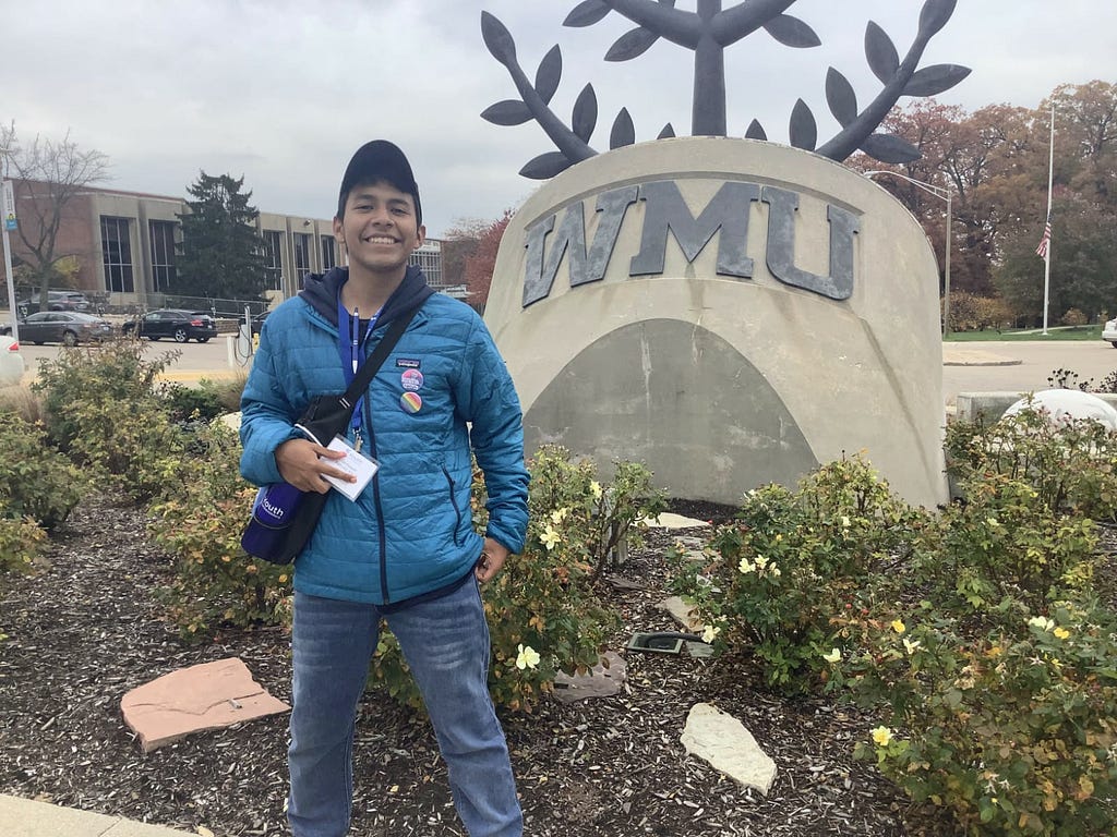 A young adult stands in front of a statue with the letters “WMU” on it.