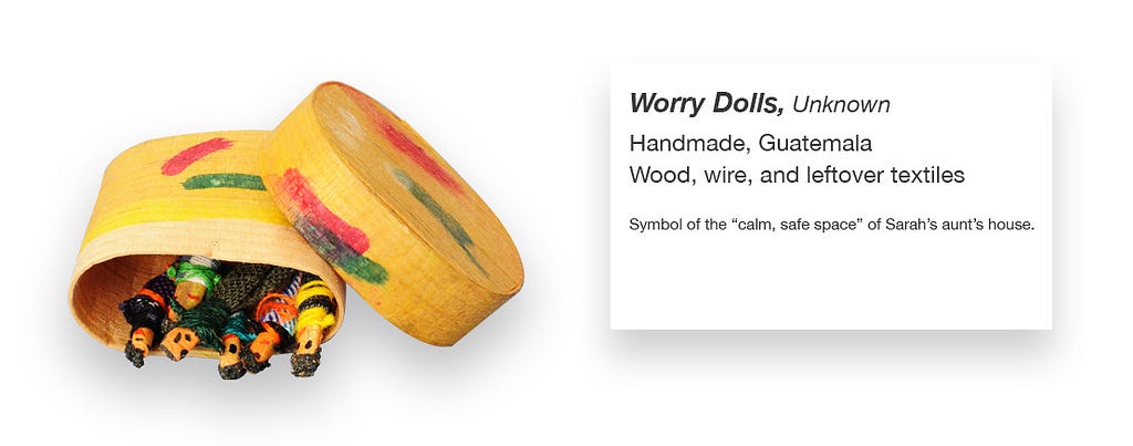 A yellow box of worry dolls with what looks like a museum label with the following text: Worry Dolls, Unknown; Handmade, Guatemala; Wood, wire, and leftover textiles; symbol of the “calm, safe space” of Sarah’s aunt’s house