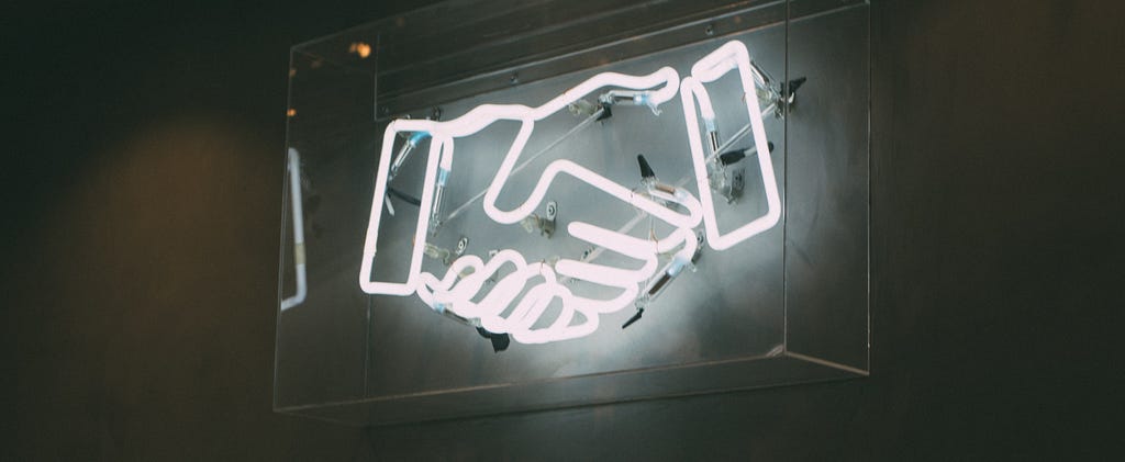 Neon light display creating the outline of a handshake