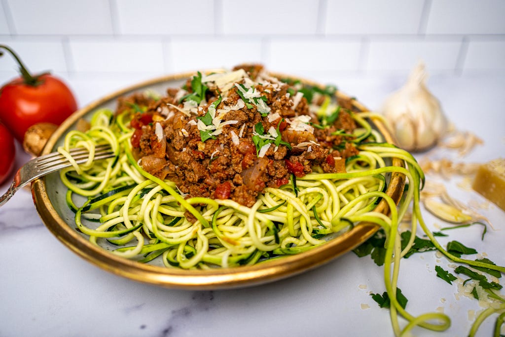 A bowl of zucchini noodles with an Italian ground beef and tomato sauce on top.